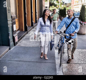 Business man and woman walking in street, man pushing bike, smiling Stock Photo