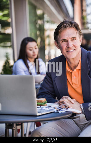 Businessman sitting outside cafe, using laptop Stock Photo