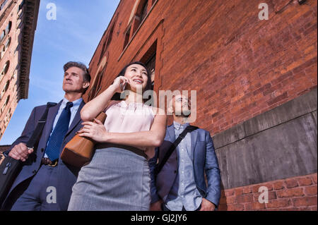 Businessmen and women walking outdoors, using smartphone, low angle view Stock Photo