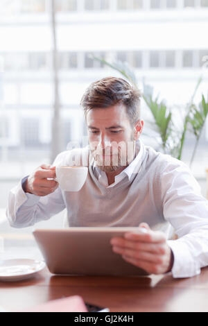 Mature man sitting in cafe, drinking coffee, using digital tablet Stock Photo