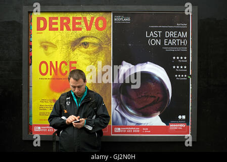 A man using his mobile phone and standing in front of Edinburgh Fringe Festival posters. Stock Photo