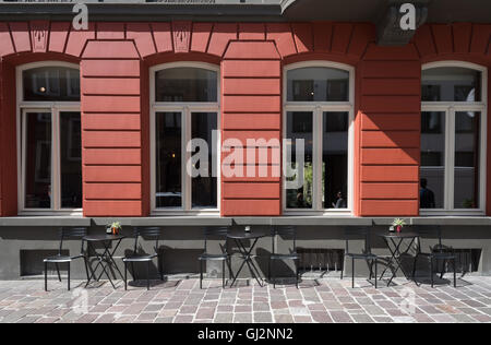 Repeated lines, shapes and windows on a striking red facade.  Repeated outdoor tables and chairs in the foreground. In Bruges. Stock Photo