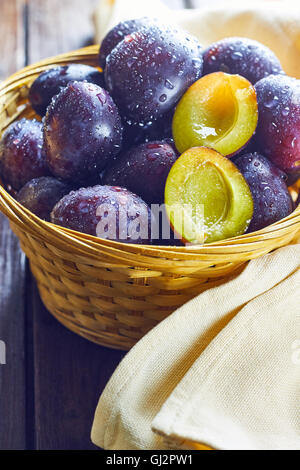 Fresh plums in weaved basket on wooden table Stock Photo