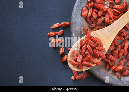 Dried goji berries in wooden spoon on black background. Top view with copy space Stock Photo