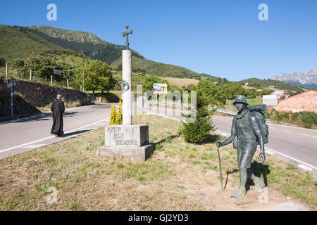 Priest in background and cross with statue of walker symbolizing hiking camino to Santiago.Famous pilgrimage trail near Potes. Stock Photo