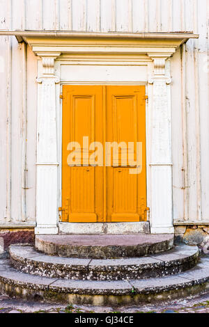 Old and weathered yellow double door without handle on a white house. Stock Photo