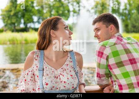 Young woman leaning on railing of the wooden gazebo standing in front of human-made waterfall with her boyfriend in a park with Stock Photo