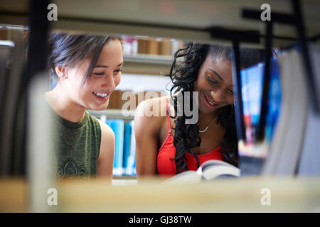 Two young female college students reading book on library shelves Stock Photo