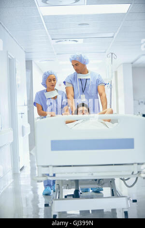 Doctors wearing surgical scrubs pushing patient in hospital bed Stock Photo