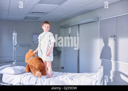 Portrait of boy patient on bed holding teddy bear on hospital children's ward Stock Photo
