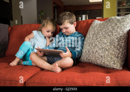 Siblings using digital tablet on sofa Stock Photo