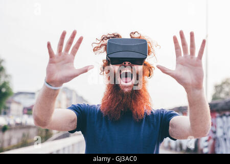 Portrait of young male hipster with red hair and beard screaming whilst wearing virtual reality headset Stock Photo