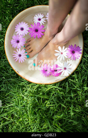 Young woman's feet in bowl of flower water on lawn Stock Photo