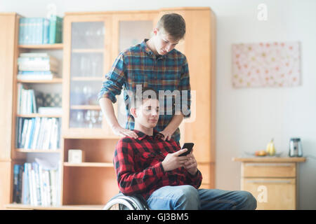 Young man using wheelchair reading smartphone texts in kitchen Stock Photo