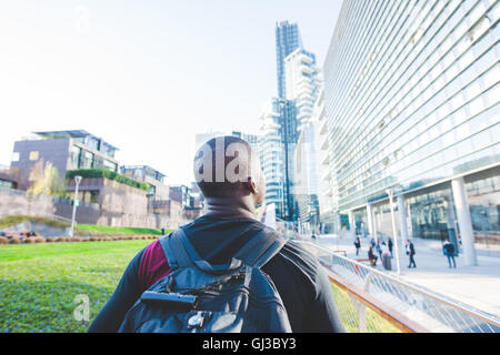 Young man walking outdoors, wearing backpack, rear view Stock Photo