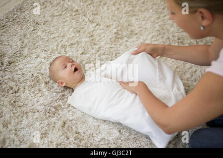 Swaddling Step 5. Mother wrapping and tucking in baby boy with blanket Stock Photo