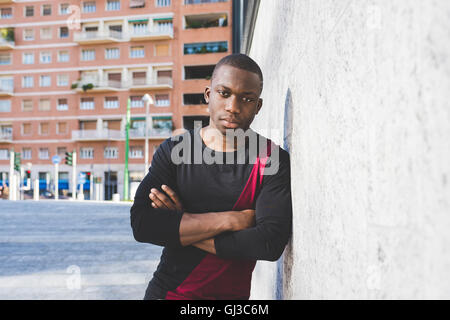 Portrait of young man leaning against wall, arms folded, pensive expression Stock Photo