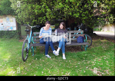 Young adult sisters with bicycles sitting on bench looking at map Stock Photo