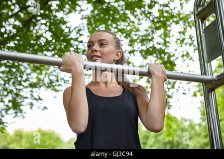 Young woman training in park, doing chin ups on exercise bars Stock Photo