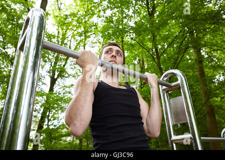 Young man training in park, doing chin ups on exercise bars Stock Photo