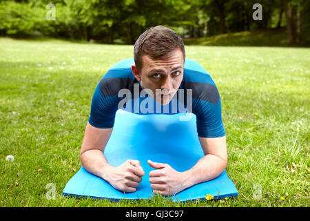 Young man training in park, doing push ups on exercise mat Stock Photo