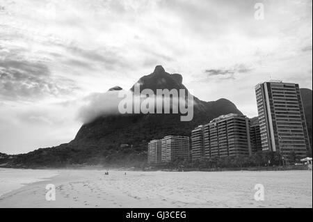 Dramatic monochrome view from the shore of Sao Conrado beach in Rio de Janeiro, Brazil with mist cllinging to the Pedra da Gavea Stock Photo