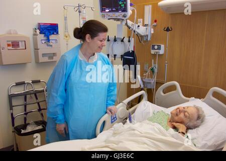 Woman visiting sick grandmother in hospital, wearing gown and gloves due to Clostridium difficile infection in older woman. Stock Photo