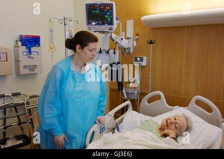 Woman visiting sick grandmother in hospital, wearing gown and gloves due to Clostridium difficile infection in older woman. Stock Photo