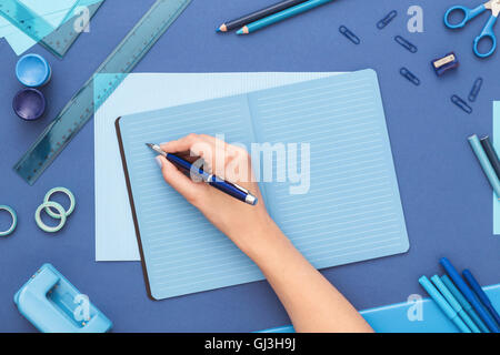 Writing in the notebook with school and office supplies on office table. View from the top. Stock Photo