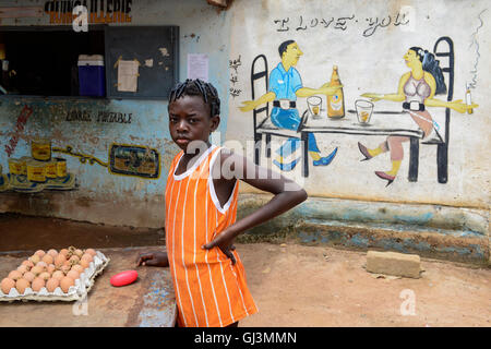 BURKINA FASO, Province Poni, Gaoua, wall painting as advertisement for beer bar, man and woman sitting at table drinking Brakina Beer, the local beer of the brewery in Burkina Faso, girl selling chicken eggs, slogan I love you and God is one Stock Photo