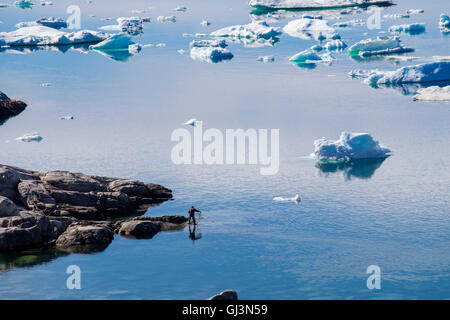 Local Inuit man fishing with a net on shore of Ilulissat Icefjord or Isfjord with icebergs in summer. Ilulissat west Greenland Stock Photo