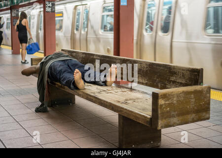 A homeless individual sleeps on a bench in a subway station in New York ...