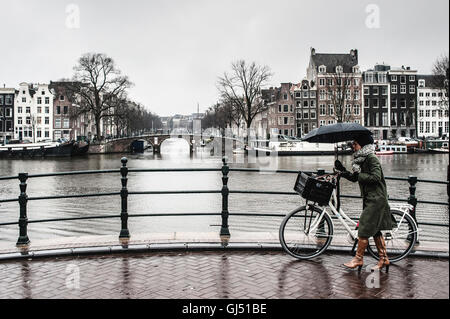 A woman with a bicycle in the rain on a bridge in Amsterdam Stock Photo