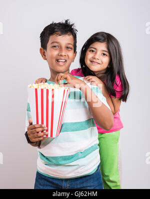 indian cute girl and boy eating popcorn, asian kids and popcorn, Little girl and little boy enjoy eating popcorn  and TV Stock Photo