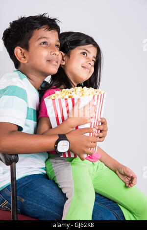 indian cute girl and boy eating popcorn, asian kids and popcorn, Little girl and little boy enjoy eating popcorn  and TV Stock Photo