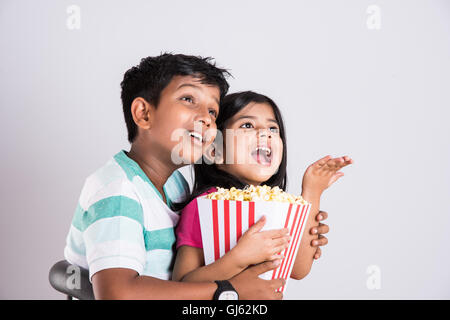 indian cute girl and boy eating popcorn, asian kids and popcorn, Little girl and little boy enjoy eating popcorn  and TV Stock Photo