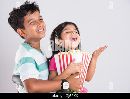 indian cute girl and boy eating popcorn, asian kids and popcorn, Little girl and little boy enjoy eating popcorn  and TV Stock Photo