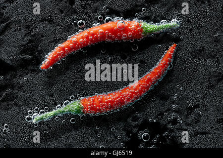 Chili pepper in a mineral water, a series of photos. Close-up carbonated water against black background Stock Photo