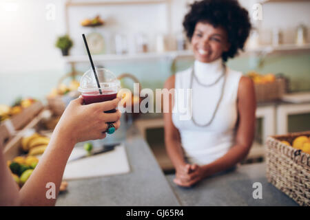 Closeup shot of glass of fresh fruit juice in hand of a customer with bartender standing behind the counter in background. Stock Photo