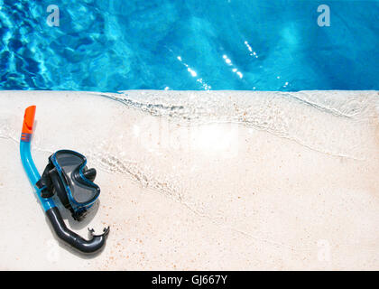 A pair swimming goggles and snorkel on a stone marble edge of a crystal clear blue pool with morning sunlight reflecting Stock Photo