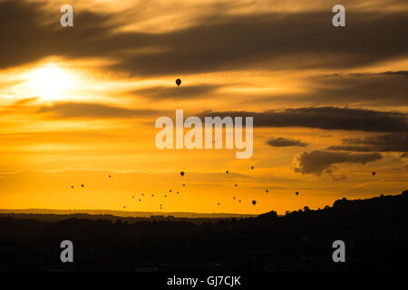 Fleet of hot air balloons in front of sunset. Mass launch at annual Bristol Balloon Fiesta drifts towards the city of Bath Stock Photo