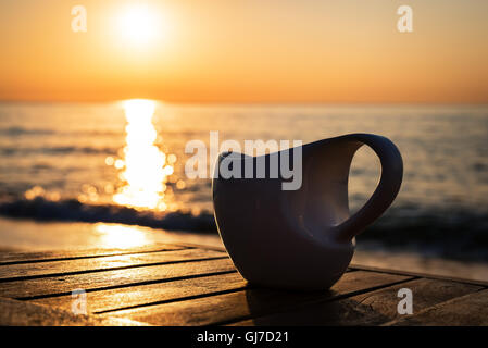 Coffee cup on wood table at sunset or sunrise beach Stock Photo