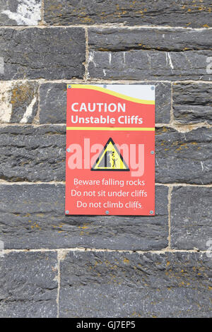 Warning information sign 'Caution unstable cliffs' on a sea wall Stock Photo