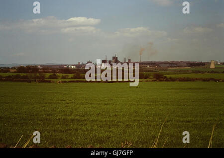 1975 blue sky view, looking north across farmland fields from Long Edge Lane, towards the smoking red iron oxide chimneys of the Consett Steelworks, closed in 1980 and now demolished, County Durham, North East England, UK Stock Photo