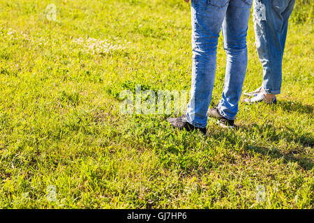 stylish couple legs on sunny grass in meadow in summer, travel together concept, space for text Stock Photo