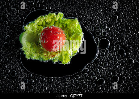 Lettuce and tomato in mineral water, a series of photos. Close-up carbonated water against black background Stock Photo
