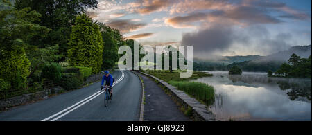 A cyclist enjoys dawn breaking over Rydal Water, English Lake District, Cumbria, UK.