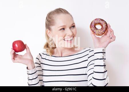 MODEL RELEASED. Pregnant woman holding apple and doughnut. Stock Photo