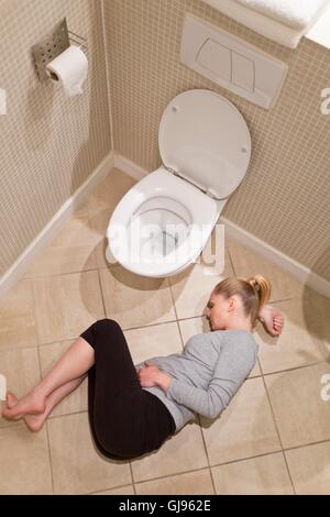 MODEL RELEASED. Pregnant woman lying on bathroom floor by toilet. Stock Photo