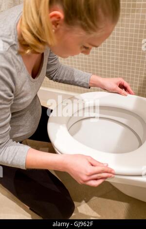 MODEL RELEASED. Pregnant woman with morning sickness kneeling over toilet. Stock Photo